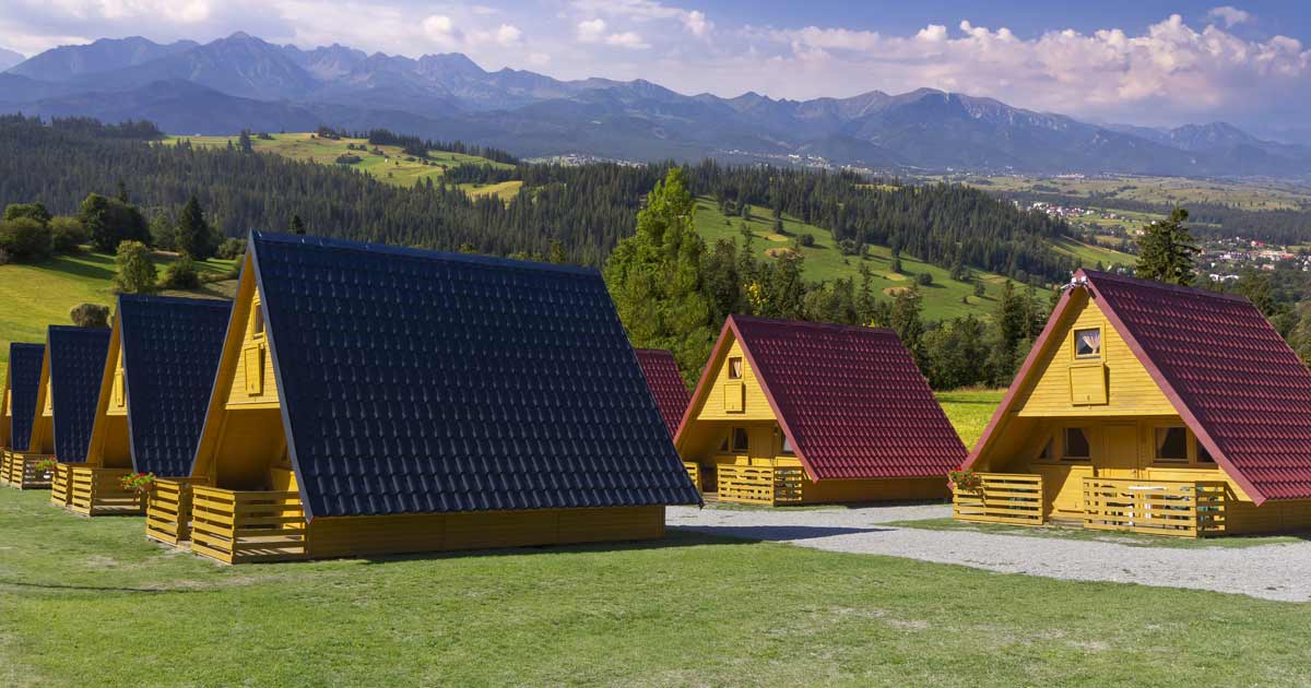 A-frame camp cabins on a hillside with mountain backdrop at a summer camp rental facility