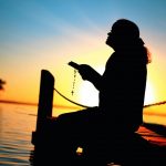 Person praying on a waterfront dock at sunset at a summer camp religious retreat