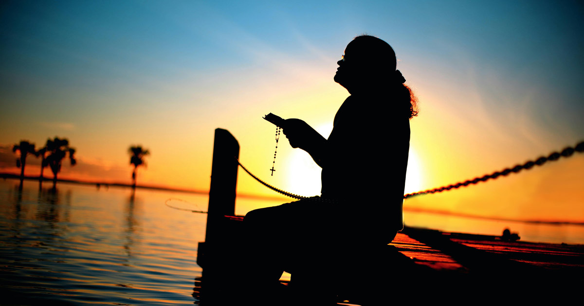 Person praying on a waterfront dock at sunset at a summer camp religious retreat