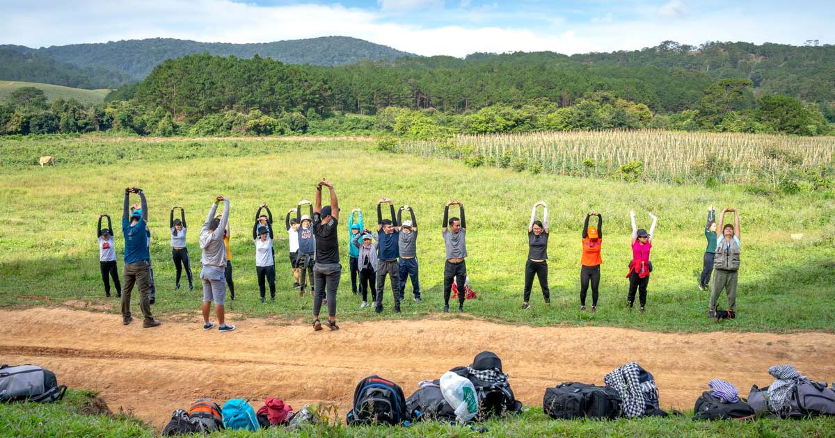 Athletic team gathered for an outdoor warm-up on open field at a summer camp, gear bags in foreground